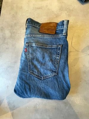  Levi's jeans  - Säljer ett par blå jeans från Levi's med klassisk femficksdesign och slim passform. Jeansen har den ikoniska röda Levi's-taggen på bakfickan och en brun läderpatch i midjan. Tillverkade i slitstark denim, perfekta för en avslappnad stil. 🤩 Skriv vid minsta fråga!  STORLEK: W31 L34.      (Bilderna på jeansen kan vara lite otydliga eftersom min mobil har lite fel på kameran.)