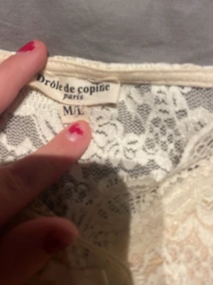 Vit spetslinne från Drôle de Copine - Supersött vitt spetslinne från Drôle de Copine Paris. Linnet har breda axelband, v-ringning och en liten rosett framtill. Hela toppen är täckt av vacker spets och har en feminin, romantisk vibe. Perfekt att styla med jeans eller kjol. Storlek L/m men skulle säga att den passar s också
