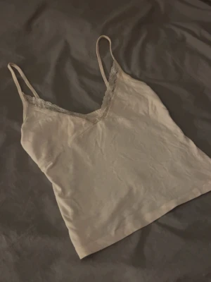 Ljusrosa linnetopp med spets - Säljer en ljusrosa linnetopp med tunna axelband och v-ringning. Toppen har fina spetsdetaljer längs halsen och är tillverkad i mjukt bomullsmaterial. Perfekt att matcha med jeans eller kjol för en enkel och snygg look.