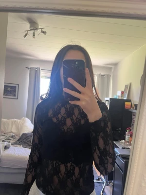 Svart spetsblus med lång ärm - svart spetsblus med lång ärm och transparent mönster. Blusen har en figurnära passform och hög hals.