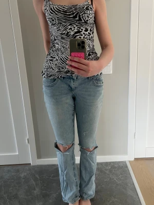 Ljusblå slitna jeans med hål - Säljer ett par ljusblå jeans med raka ben och stora slitningar vid knäna. Jeansen har klassisk femficksdesign och är tillverkade i denim. Perfekt för dig som gillar en avslappnad och trendig look. (Har defekter!)