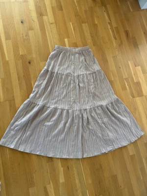 Lång kjol - Superfin, randig maxikjol med volanger och knappdetaljer fram. Bekväm elastisk midja. Perfekt för sommaren!