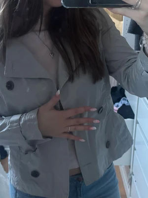 Kort grå trenchcoat med knappar - SNYGGASTE trenchcoaten, älskar den verkligen men är för liten för mig tyvärr. Storlek 38 så S/M, fint skick finns inget band men märks inte. Skriv för frågor☺️