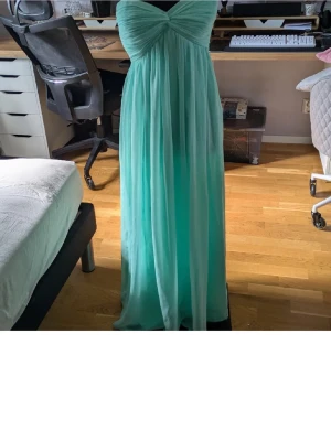 Ljusblå axelbandslös långklänning - Säljer en elegant ljusblå långklänning med axelbandslös design och draperad överdel. Klänningen har ett svepande fall och är perfekt för speciella tillfällen. Materialet känns lätt och luftigt, vilket ger en fin siluett.