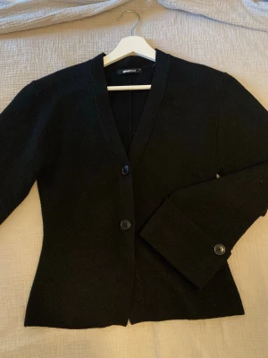 Svart kofta från ginatricot  - Stilren svart kofta från ginatricot. Koftan har långa ärmar och en figurnära passform. Perfekt att slänga över en topp för en enkel och snygg look. Kommer från ett djur och rökfritt hem. Använd endast tre gånger.