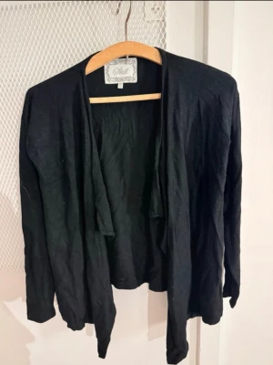 Svart öppen kofta från skill - Snygg svart öppen kofta från skill med lång ärm och avslappnad passform. Koftan har ett tunt, mjukt tyg och faller snyggt framtill utan knäppning. Perfekt att slänga över en t-shirt eller topp för en chill look.