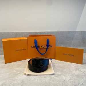  bälte -  Snyggt bälte i svart med  klassiskt monogrammönster och logga i svart på spännet. Bältet är 105 cm. Bältet har en stilren, modern look som passar till jeans eller kostym. Kommer med originalpåse, ask och kvitto. Bara att höra av er om ni har någon fråga eller vill ha fler bilder.           Pris går att diskuteras