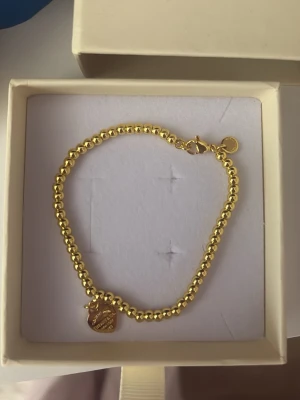 Guldarmband  - Snyggt armband i guldfärgat material från Tiffany c.o , med små runda pärlor och ett hjärtformat hänge. Lås med karbinhake och extra rund bricka vid låset. Fått i present för något år sen har ej något kvitto är i ett mycket bra skick använt fåtal gånger 