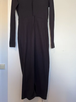 Svart långärmad långklänning - En svart långklänning med lång ärm och enkel, stilren design. Klänningen har en lätt textur i tyget och rak passform som ger en elegant siluett. Perfekt för dig som gillar minimalistisk stil.