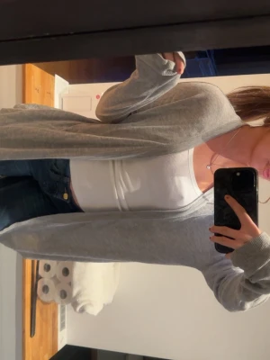 Ljusgrå lång kofta i mjukt material - Säljer en ljusgrå, lång och öppen kofta med långa ärmar. Koftan är tillverkad i ett tunt och mjukt material som känns skönt mot huden. Perfekt att slänga över en topp för en avslappnad look.