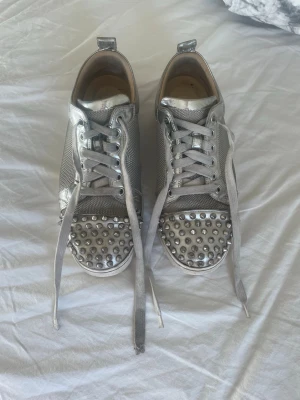 Silvriga sneakers med nitar - Christian Louboutin sneakers – strl 38  Säljer mina snygga silverfärgade Christian Louboutin sneakers med nitar. Väldigt statement-skor som verkligen sticker ut ✨  Storlek: 38 Skick: Använda men fortfarande i bra skick. Finns tecken på slitage (se bilder): – repor/veck i materialet – slitage på hälen och insidan – sulorna använda (klassiska röda sulor syns fortfarande)  Ingår: Original låda + dustbag Kvitto: Finns tyvärr inte  Perfekta om du vill ha ett par Louboutins till ett bättre pris 💸