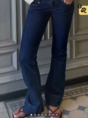 Mörkblå bootcut jeans med låg midja - Snygga mörkblå bootcut jeans med låg midja och klassiska fem fickor. Jeansen har utsvängda ben och synliga sömmar. Perfekta för en trendig och avslappnad look.