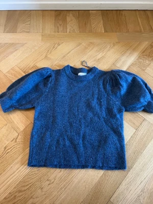 Blå stickad tröja från Gina Tricot - Mysig blå stickad tröja från Gina Tricot med puffiga trekvartsärmar och ribbade muddar. Perfekt för dig som gillar en enkel men trendig look. Rund halsringning och mjukt material som känns skönt mot huden.