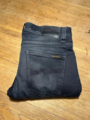 Svarta Nudie Jeans - Säljer ett par svarta jeans från Nudie Jeans med klassisk femficksdesign och diskret logga på  bakfickan. Inte använda så mycket tvättade några gånger model Lean Dean 