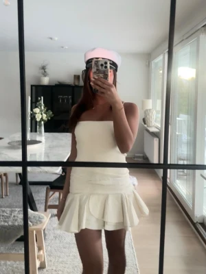 Vit kort klänning med volang - student - Zara  - Säljer en snygg vit kort klänning med volang nertill och axelbandslös design. Perfekt för student eller sommarens alla tillfällen. Klänningen har en figurnära passform och är tillverkad i ett mjukt bomullsmaterial. Ny från Zara med prislapp storlek S finns inte att köpa längre. Super fin till studenten, midsommar. 💓💓💓