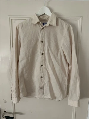 Beige line skjorta från Jack & Jones - Stilren beige line skjorta från Jack & Jones. Klassisk krage, långa ärmar och knappar framtill. Perfekt för en clean och enkel look. Passar till det mesta och är lätt att matcha med andra plagg.