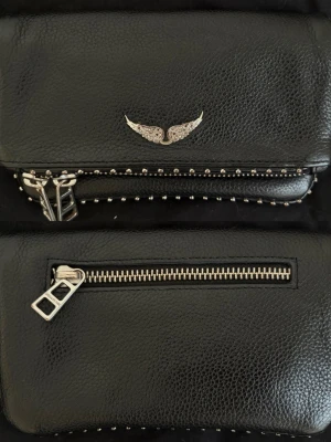 Svart Zadigväska! - Cool svart axelremsväska från Zadig med silvriga nitar runt kanterna. Väskan har dragkedjor och detaljer i silver och en extra ficka på baksidan. Sparsamt använd. 