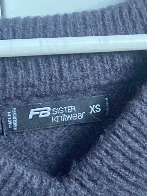 Mörkgrå stickad tröja FB Sister XS - Mysig mörkgrå stickad tröja från FB Sister i storlek XS. Tröjan har en djup V-ringning och är tillverkad i ett fluffigt, mjukt material. Perfekt för lager-på-lager och passar till både jeans och kjol.