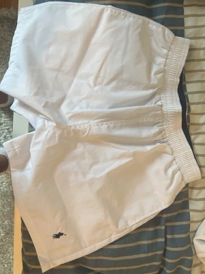 Vita shorts från Polo Ralph Lauren - Klassiska vita shorts från Polo Ralph Lauren med elastisk midja och liten broderad logga på benet. Shortsen har en bakficka och är perfekta för sommaren. Snygg och enkel design som passar till det mesta.