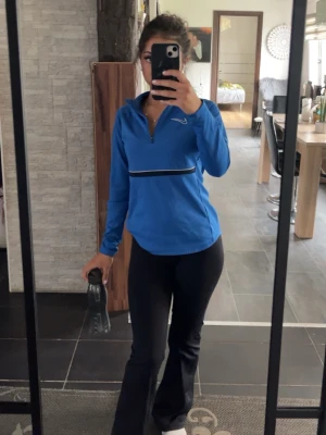 Blå träningströja från Nike - Snygg blå långärmad träningströja från Nike med halv dragkedja framtill och vit logga på bröstet. Tröjan har en svart och vit rand över bröstet och är tillverkad i ett stretchigt funktionsmaterial som passar perfekt till träning.