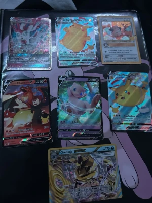 Pokémon TCG holografiska samlarkort - Säljer ett set med sex holografiska Pokémon TCG-kort, inklusive Charizard V, Mew V, Greninja, Flying Pikachu VMAX, Surfing Pikachu VMAX och fler. Korten har färgstarka illustrationer och glansig finish, perfekta för samlare eller Pokémon-fans.