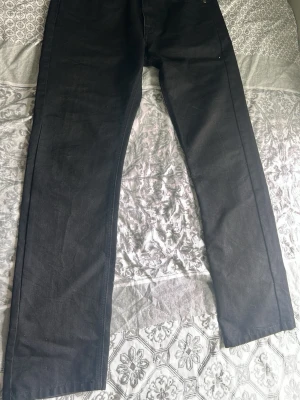 Svarta raka jeans från Dressmann - Säljer ett par svarta jeans från Dressmann med rak passform. Jeansen har klassisk design med fem fickor och är tillverkade i ett mjukt och slitstarkt material. Perfekta för dig som gillar en stilren och enkel look.