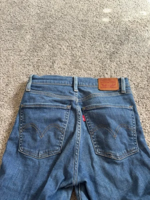 Levi's blå raka jeans - Klassiska blå Levi's jeans med raka ben och fem fickor. Jeansen har en ikonisk läderpatch bak i midjan och den röda Levi's-taggen på bakfickan. Tillverkade i slitstark denim med snygga kontrastsömmar och bälteshällor. Liten tråd som har gått upp kika på sista bilden . 