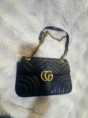 Elegant väska - Säljer en supersnygg och rymlig handväska i läder med guldfärgade detaljer och kedjerem. Perfekt storlek för det viktigaste och ger en lyxig touch till din outfit. Den har spår av användning, vänligen titta noga på bilderna. Då det är en begagnad vara sker försäljningen i befintligt skick. 