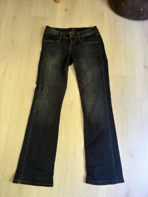 Bootcut jeans i mörk denim - Snygga bootcut jeans från LTB i mörkblå denim med slitningar framtill i tvätten och kontrastsömmar. Klassisk femficksmodell och låg midja. Perfekta till sneakers eller boots för en avslappnad look. Storlek W28/L32