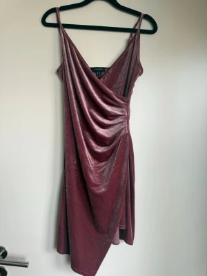 Rosa asymmetrisk sammetsklänning - Säljer en rosa kortklänning i mjuk sammet. Klänningen har smala axelband, omlott framtill med draperad effekt och asymmetrisk nederkant.