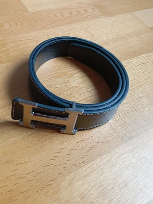 H%M bälte - Snyggt svart bälte från med ett H, den har stiliga och snygga vita sömmar i kanterna, detta bälte kan enkelt lyfta vilket outfit som helst.