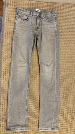 Ljusgrå skinny jeans från 157 - Snygga ljusgrå skinny jeans från 157 med klassisk femficksdesign och diskreta slitningar. Jeansen har smal passform och normal midja, perfekta till en avslappnad streetstil. Tillverkade i stretchigt denim för extra komfort.