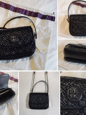 Svart quiltad handväska Tory Burch - Snygg svart quiltad handväska från Tory Burch i glansigt läder. Väskan har ett elegant mönster, guldfärgade detaljer och kedjerem. Logotypen syns framtill och insidan har dragkedjefack. Perfekt för dig som vill ha en trendig och stilren accessoar.