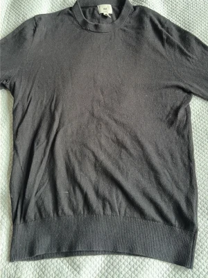 Svart stickad tröja från H&M - En enkel och stilren svart stickad tröja från H&M med rund halsringning och långa ärmar. Tröjan har ribbade muddar vid ärmslut och nederkant. Perfekt basplagg till garderoben och lätt att matcha med olika stilar. Det finns ett hål i höger armhåla som men ser på bild nummer 3. 