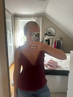 Vinrött spetslinne - Topp med smala axelband och spetsdetaljer längs urringningen. Liten rosett framtill och mjukt, stretchigt material som känns skönt mot huden. 