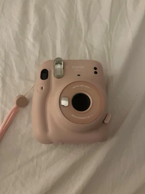 Rosa Fujifilm Instax Mini 11 kamera - Säljer en rosa Fujifilm Instax Mini 11 direktbildskamera. Kameran har en kompakt och rundad design i plast, inbyggd blixt och enkel knapp för att ta bilder. Perfekt för att skriva ut foton direkt och fånga ögonblicken med vänner.