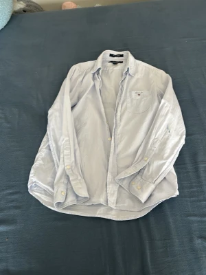 Ljusblå skjorta från GANT - Klassisk ljusblå skjorta från GANT med bröstficka och broderad logga. Skjortan har lång ärm, knappar framtill och en avslappnad passform. Perfekt till jeans eller chinos för en clean och stilren look.