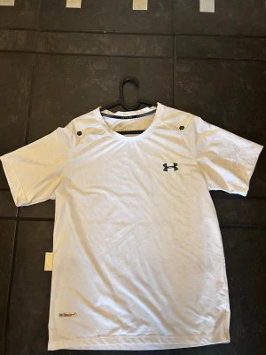 Vit t-shirt från Under Armour - Snygg vit t-shirt från Under Armour med korta ärmar och rund hals. Diskret logga på bröstet och ventilerande material som passar perfekt till träning. Klassisk passform och stilren design.