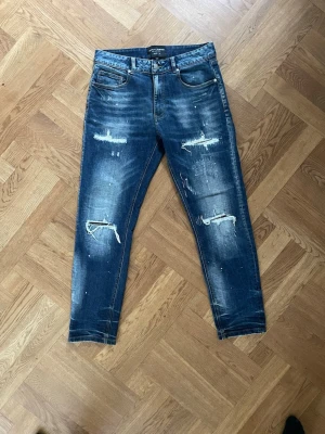 Blå slitna jeans med hål - Säljer ett par blå jeans från supply & demand med slitningar och hål på både fram- och baksida. Jeansen har en skinny fit-modell, klassiska fem fickor och coola detaljer som ger en trendig och avslappnad look. Perfekta för dig som gillar streetstyle.