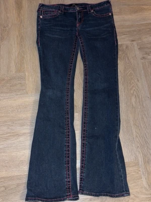 True Religion jeans med Rosa sömmar - Mörkblå jeans från True Religion med ikoniska bakfickor och kraftiga rosa kontrastsömmar. Köpta i usa och finns ej att köpa i Sverige vad jag sett, intressekoll, ni kan skriva till mig vad ni skulle va villiga att köpa de för, jag köpte dom för 2500kr