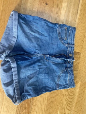 Blå jeansshorts från g perfect jeans - Säljer ett par klassiska blå jeansshorts från g perfect jeans i storlek 36. De har upprullade benslut, fem fickor och stängs med dragkedja och knapp. Perfekta till sommaren och lätta att matcha med olika stilar.