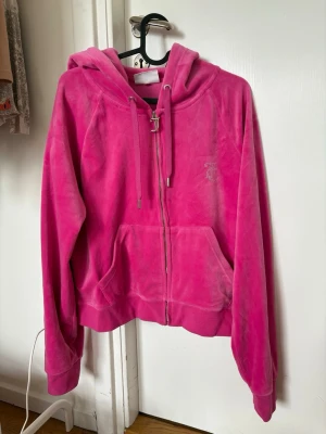 Rosa velour kofta från Juicy Couture - Juicy Couture kofta i mjuk rosa velour med dragkedja framtill, två fickor och justerbar huva med snören. Klassisk logga broderad på bröstet. 