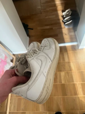 Vita Air Force 1 - Klassiska vita Nike Air Force 1 sneakers i lågt utförande. Skorna har en stilren design med perforerad tå, vit sula och ikoniska Swoosh-loggan på sidan. Tillverkade i läder med snörning och bekväm innersula.