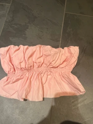 Ljusrosa bandeau topp - Söt ljusrosa bandeau topp med volangkant och resår i midjan för en bekväm passform. Toppen är axelbandslös och har en luftig, flowy känsla som passar perfekt till sommaren.