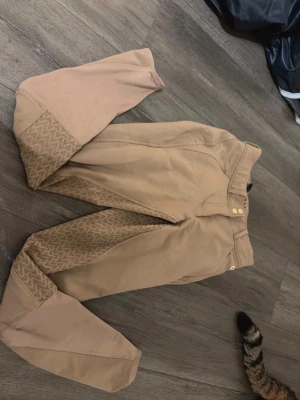 Beige ridbyxor från CRW - Säljer ett par snygga beige ridbyxor från CRW med silikonmönster på insidan av benen för extra grepp. Byxorna har två knappar i midjan, bälteshällor och fickor framtill. Perfekta för dig som gillar stilrena och funktionella ridkläder. aldrig använda!!💗