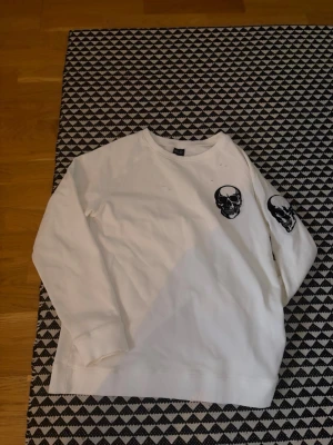 Number nine skull  - Cool vit sweatshirt från number nine med svarta döskalletryck på bröstet och ena ärmen. Tröjan har rund halsringning och är långärmad, perfekt för en edgy streetstyle-look.