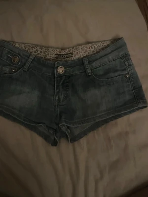 Vintage lågmidjade  jeansshorts  - Snygga blå jeansshorts från lonky med låg midja och klassisk femficksdesign. Shortsen har knapp- och dragkedjestängning samt dekorativa nitar på fickorna. Köpt i Polen på secondhand 