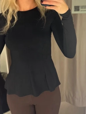 Svart långärmad topp med figurnära passform - Säljer en svart långärmad topp med rund hals och figurnära passform. Toppen har en lätt utsvängd nederkant som ger en snygg siluett. Perfekt att styla med både jeans och kjol för en clean look.