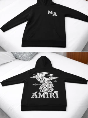 Svart hoodie från Amiri med tryck - Svart hoodie från Amiri med stor vit grafisk ängel och AMIRI-tryck på ryggen samt MA-logga på bröstet. Klassisk känguruficka framtill och huva. Tillverkad i mjukt material, perfekt för en streetwear-look.