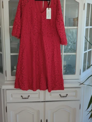 Röd spetsklänning med v-ringning - Snygg röd klänning med v-ringning och trekvartsärm. Klänningen är täckt av ett vackert spetsmönster och har en lös passform. Perfekt för dig som vill sticka ut med en färgstark look. Märke: Holly&Whyte
